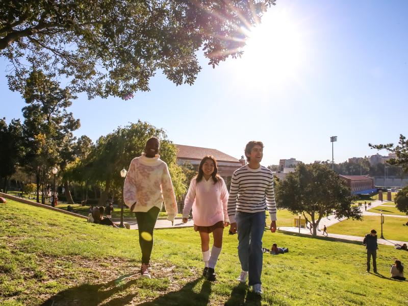 Three students walking on the UCLA campus with sun shining. 