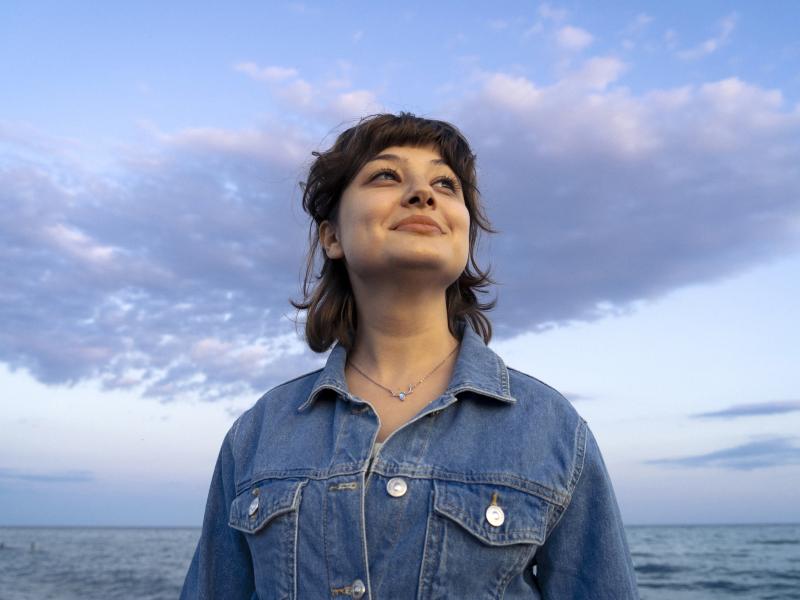 Person smiling and looking up into the sky with clouds behind them